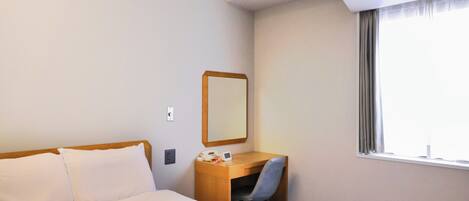 A hotel room with a bed, a desk, a chair, a mirror, and a window.