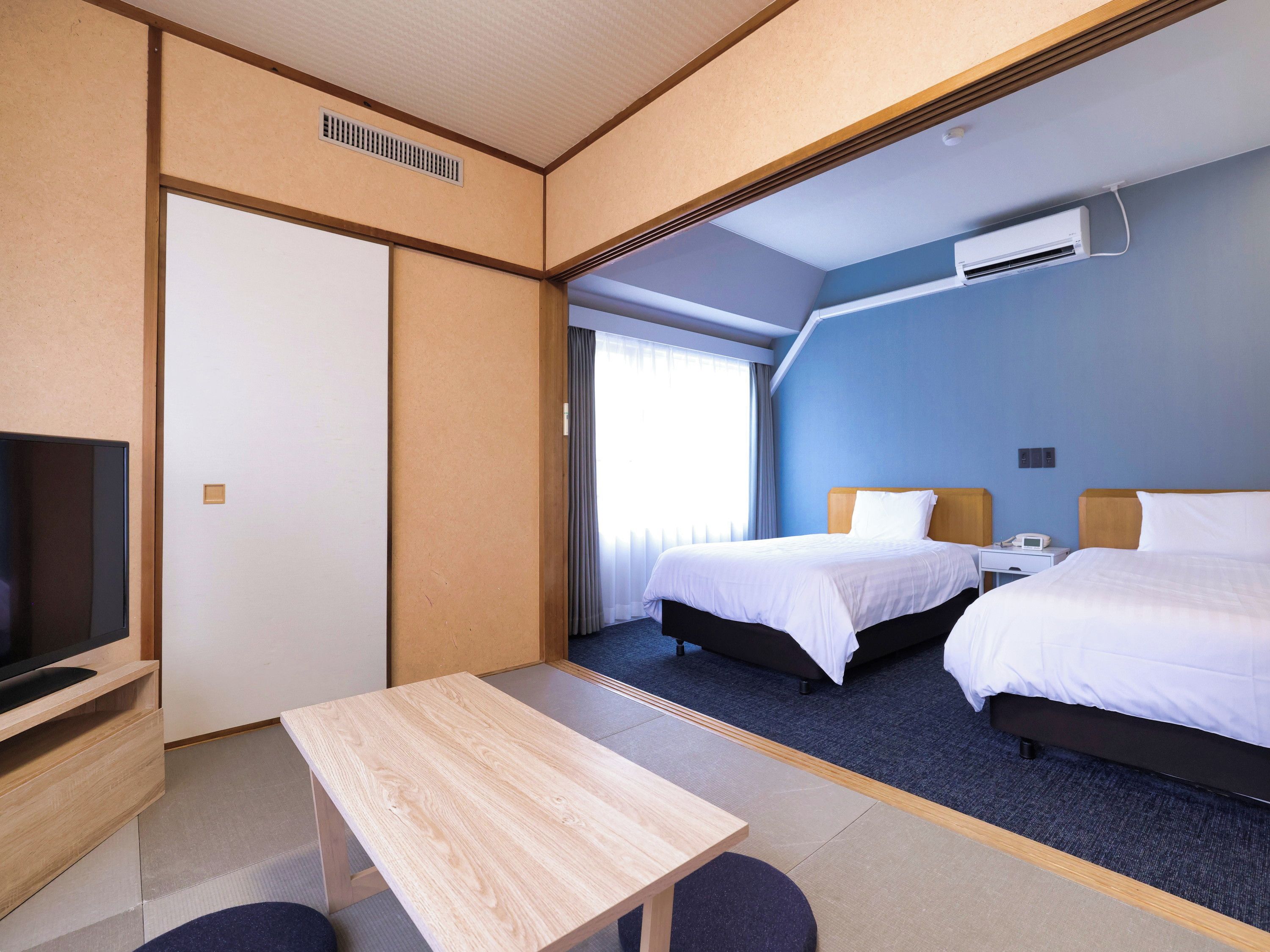 A hotel room with a bed, bedside table, TV, and a window with curtains.