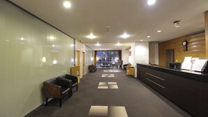 Un hall de hotel con mostrador de recepción, zona de estar y vista del hall al fondo.
