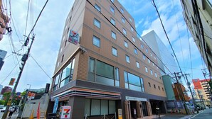 Un edificio de varios pisos con una tienda de conveniencia 7-Eleven en la planta baja, cajeros automáticos y un letrero de estacionamiento que indica servicio las 24 horas.