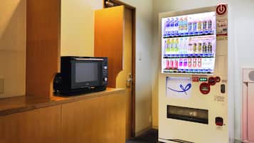 Ein Getränkeautomat mit verschiedenen Getränken und eine Mikrowelle auf einer Theke.