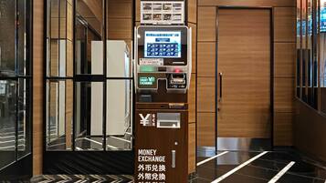A money exchange machine with a digital interface, located in a modern lobby with wooden paneling and a reflective floor.