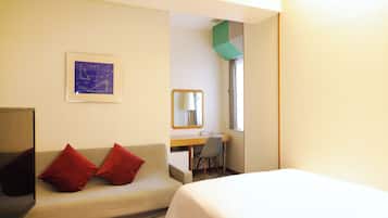 A hotel room with a bed, a desk, a chair, a television, and a couch with red cushions.