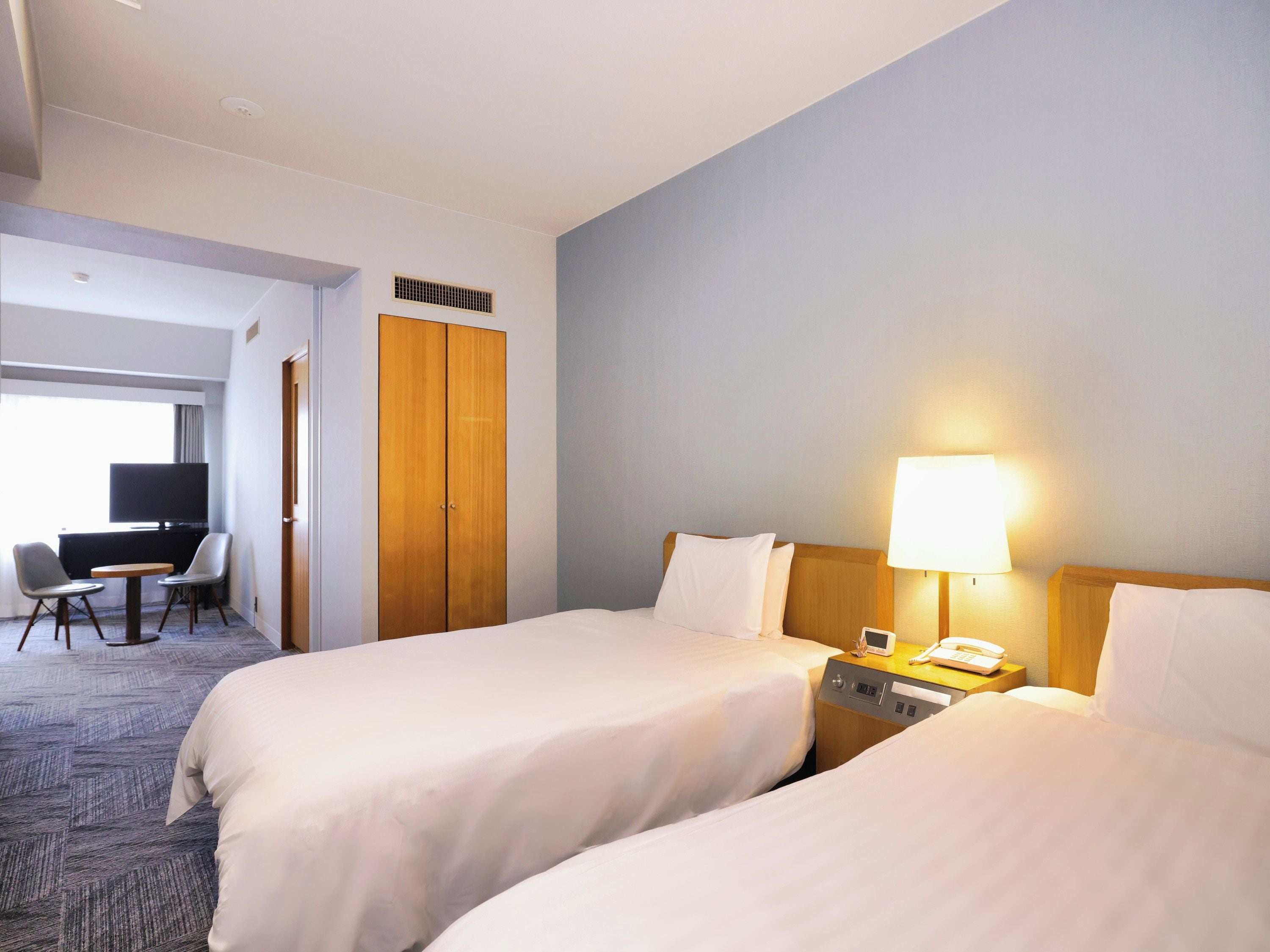 A hotel room with two beds, a desk with a chair, a television, and a lamp.