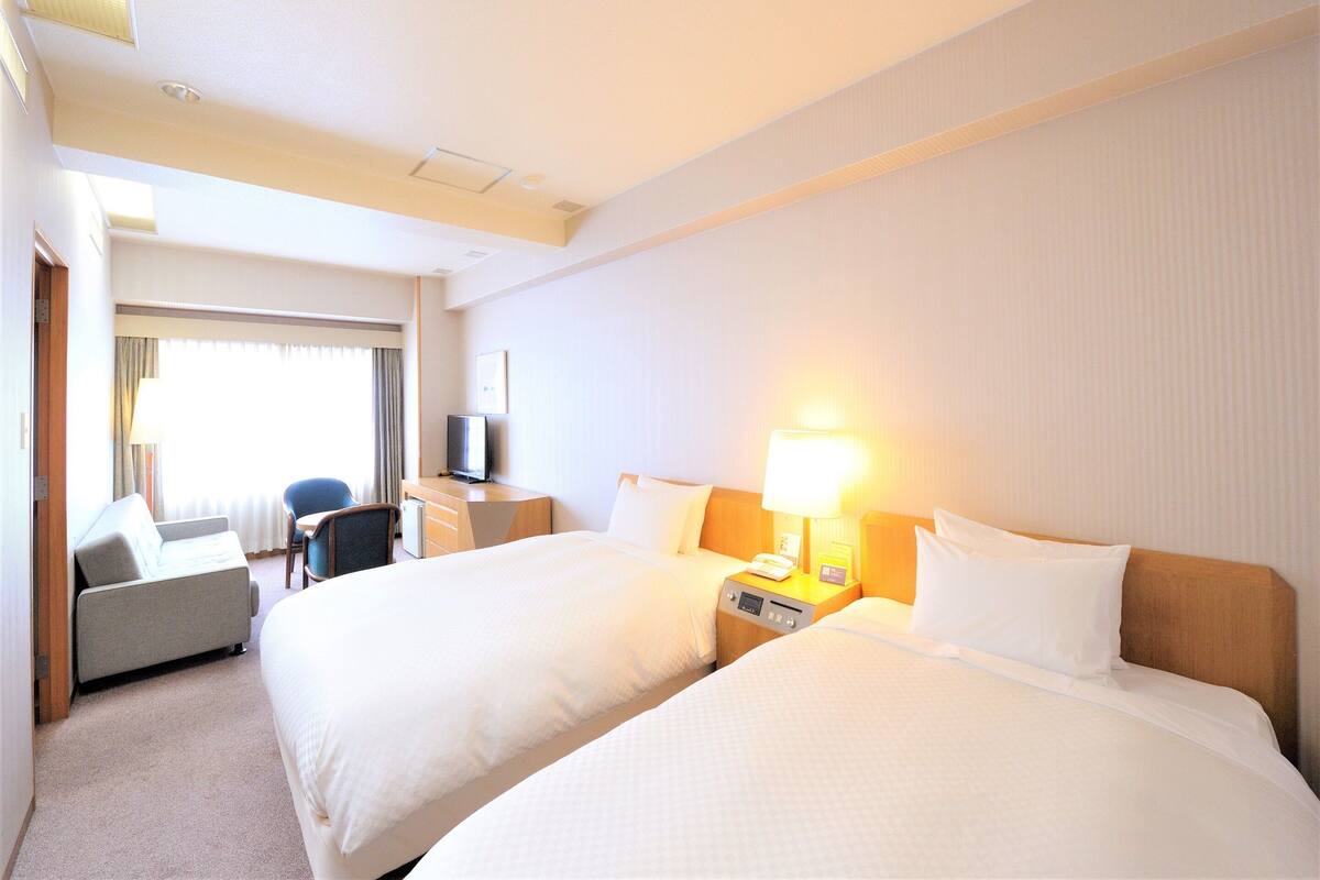 Una habitación de hotel con dos camas, un escritorio con lámpara, una silla y un televisor.