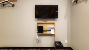 Habitación de hotel con un televisor de pantalla plana montado en la pared, un estante de madera debajo y un cubo de basura a la derecha.
