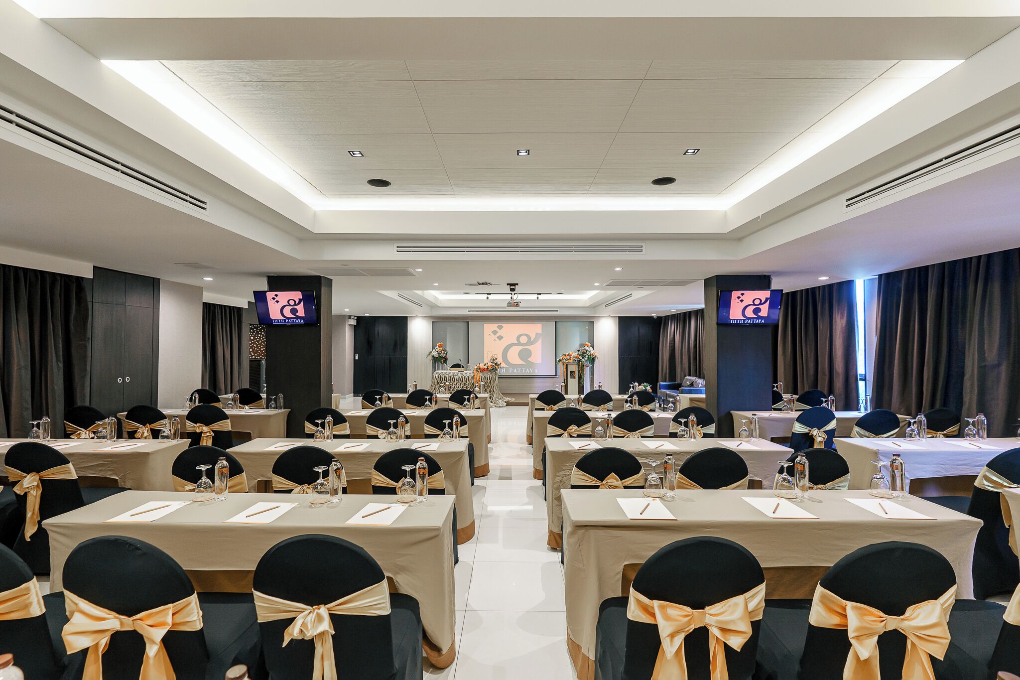 Sala de conferência com mesas preparadas para uma reunião, equipada com porta-nomes, garrafas de água e cadernos.