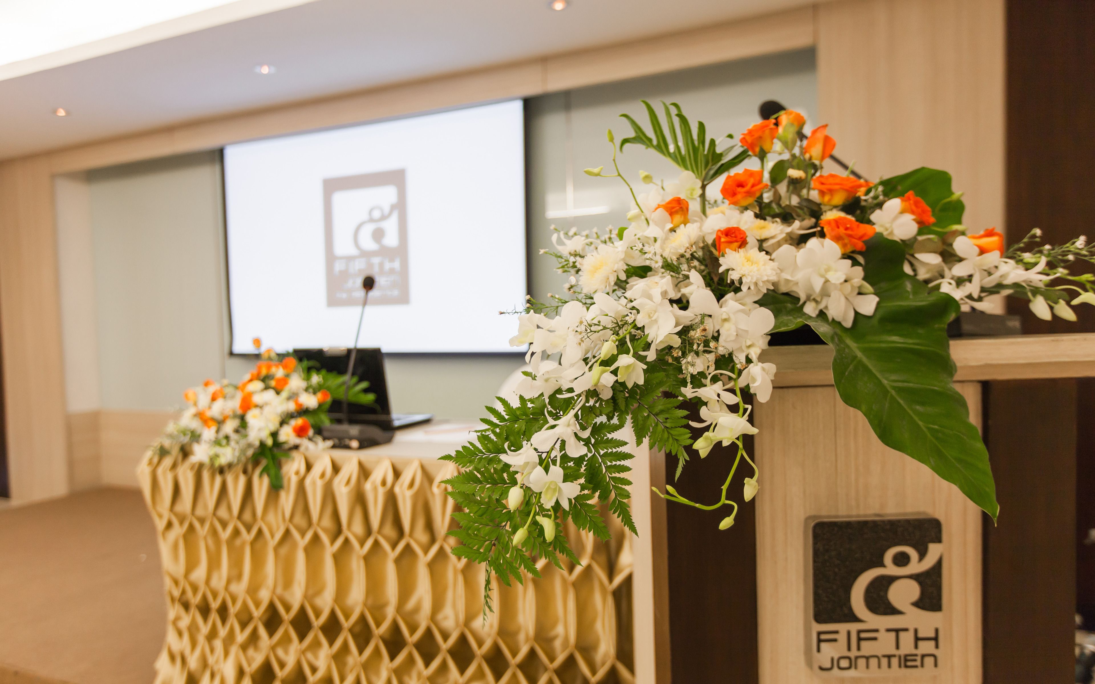 A conference room with a podium and a laptop, decorated with white and orange flowers.
