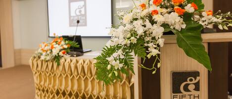 A conference room with a podium and a laptop, decorated with white and orange flowers.