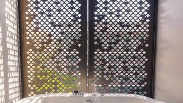Un área de spa con una bañera grande llena de agua y pétalos de rosa, techo de madera y una celosía decorativa.