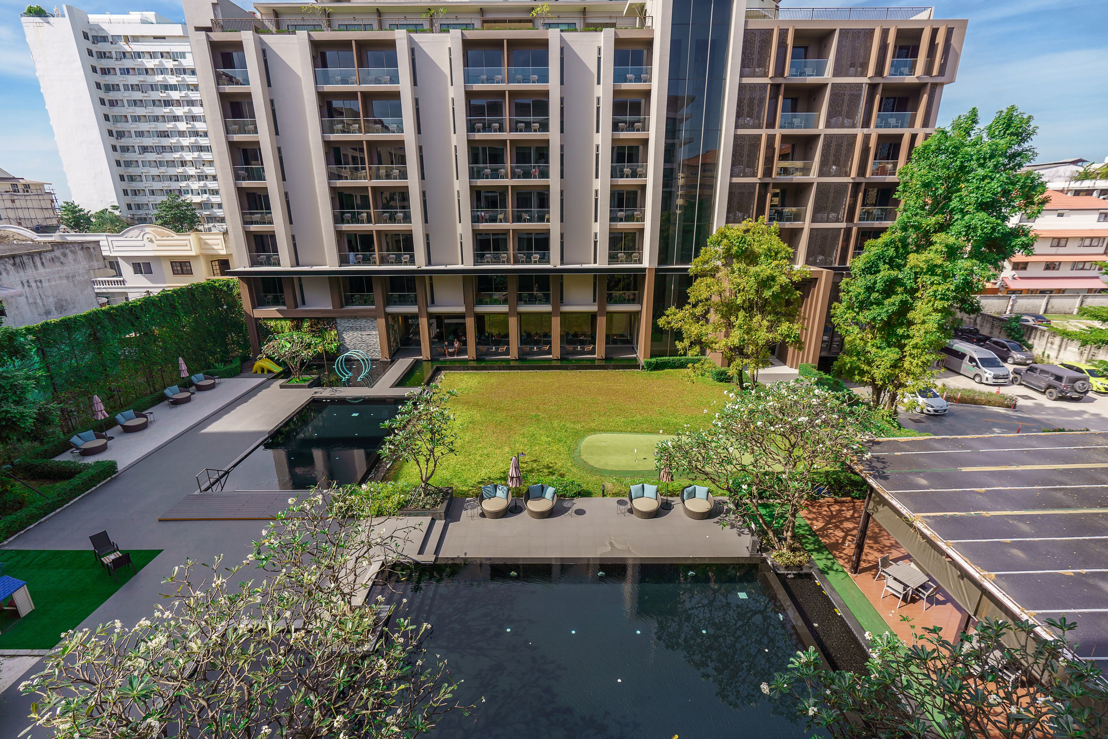Un edifici modern amb diverses plantes, una piscina al terrat i un jardí ben cuidat.