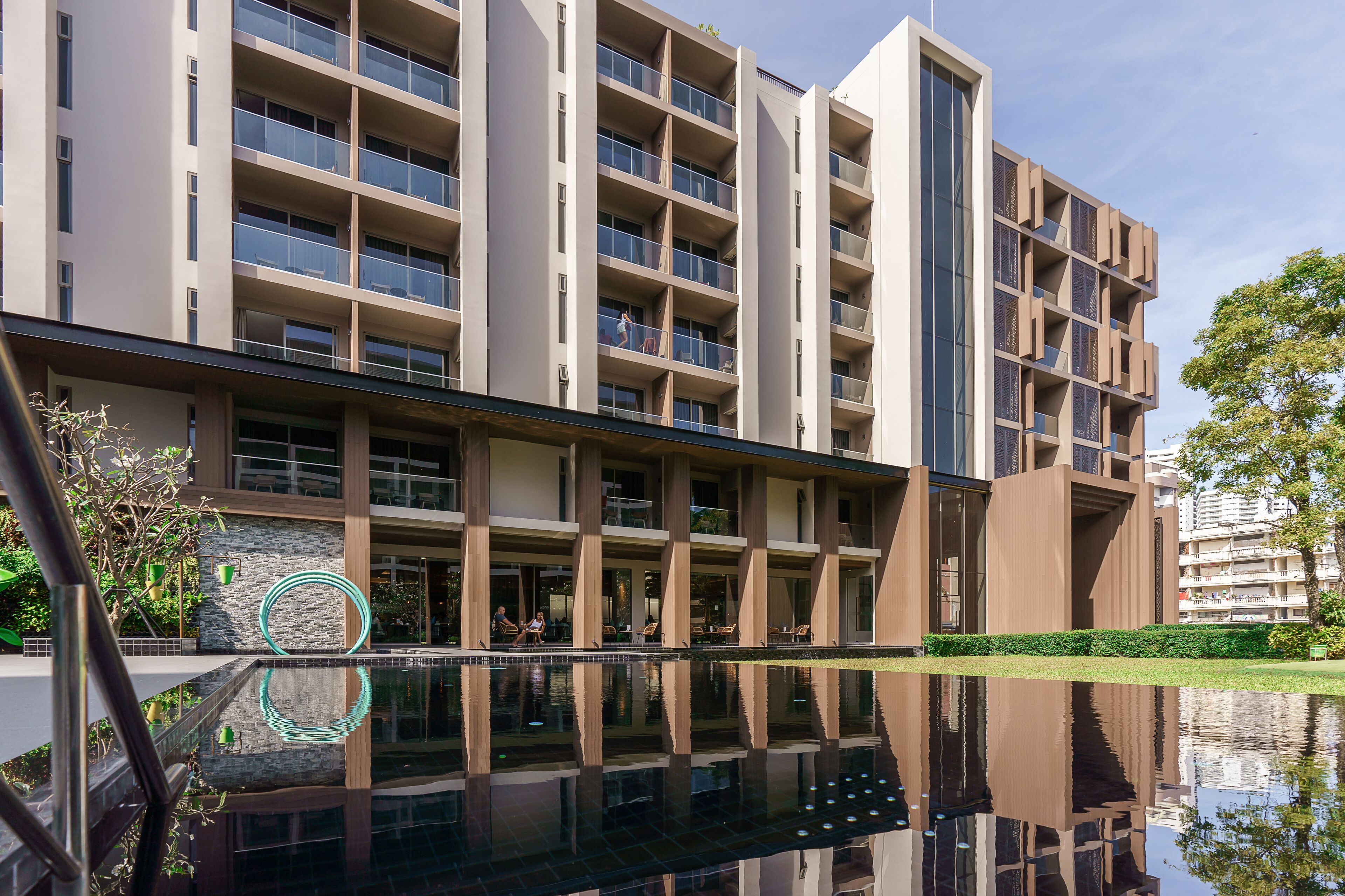 Ein modernes Mehrstöckiges Hotel mit einem spiegelnden Pool davor.