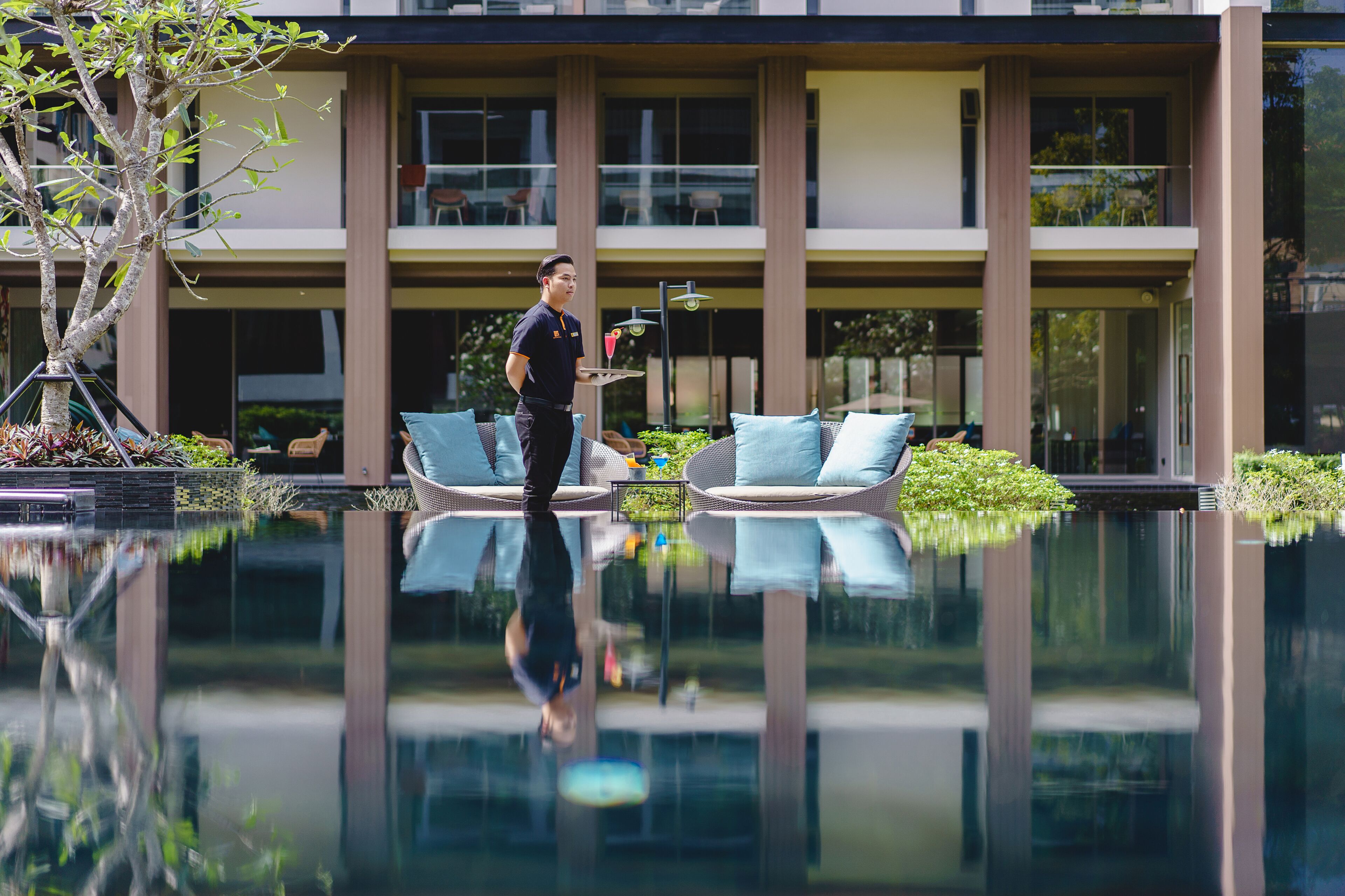Un hotel moderno con una piscina reflectante, asientos exteriores y un jardín bien cuidado.