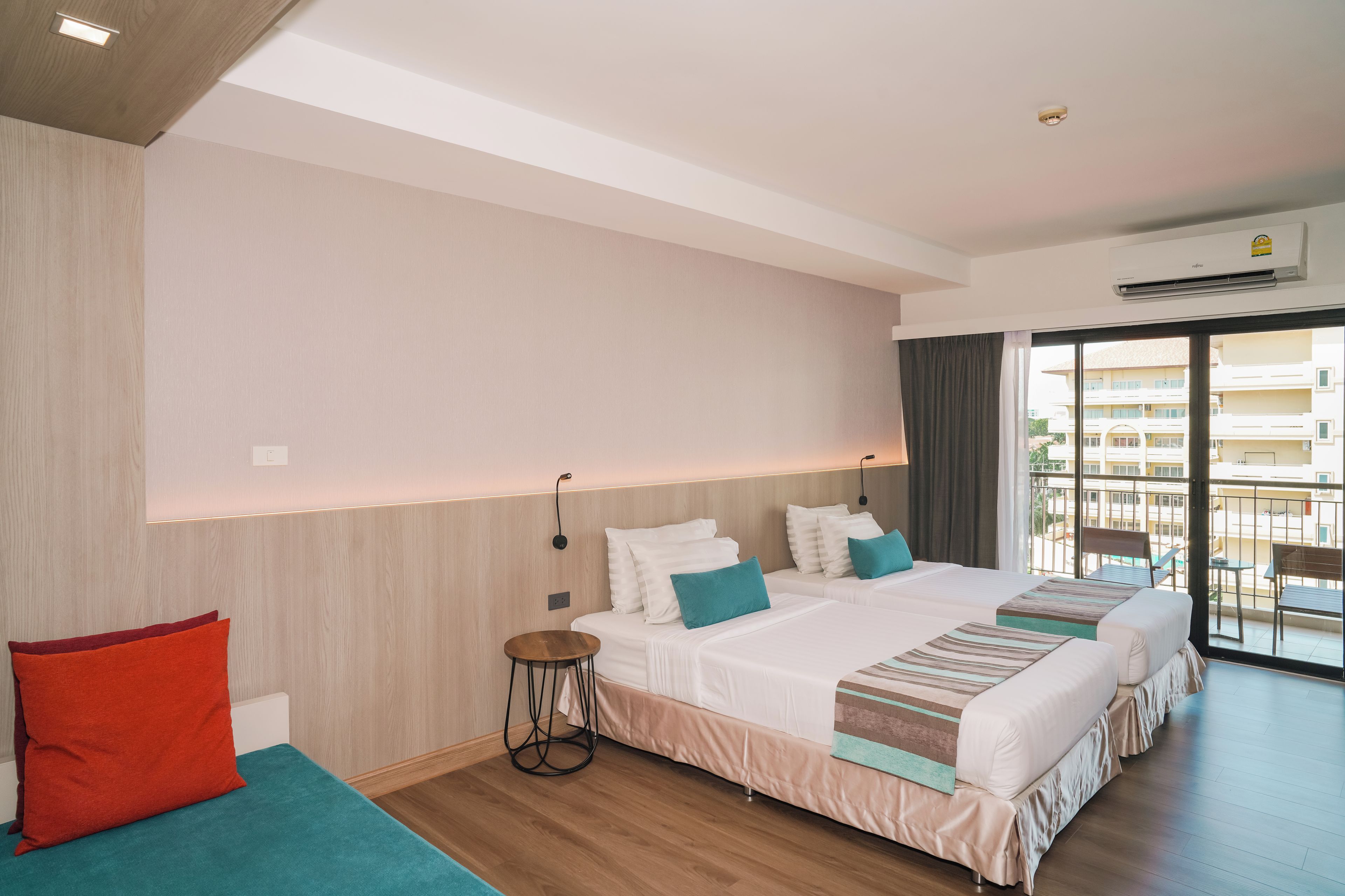 A hotel room with two beds, a small round table, and a view of the outside balcony.
