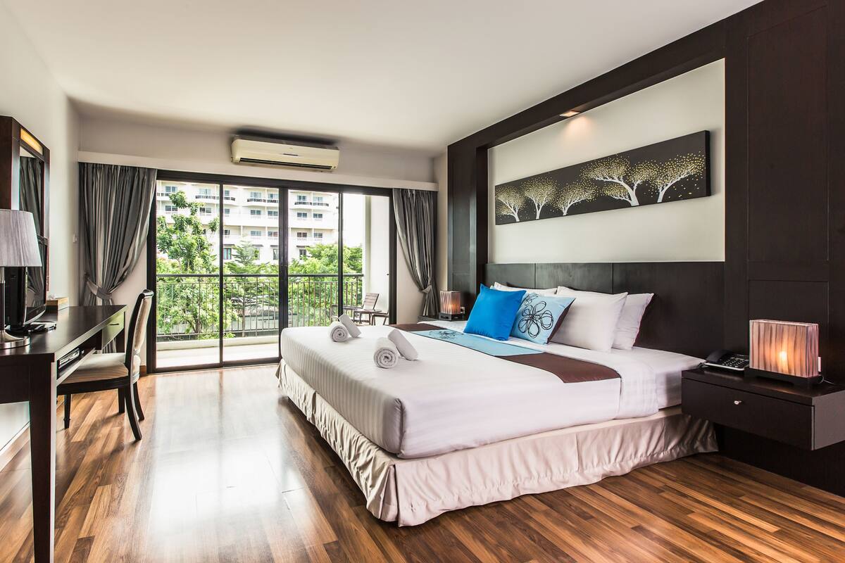 A modern hotel room with a large bed, a desk, and a view of the city.