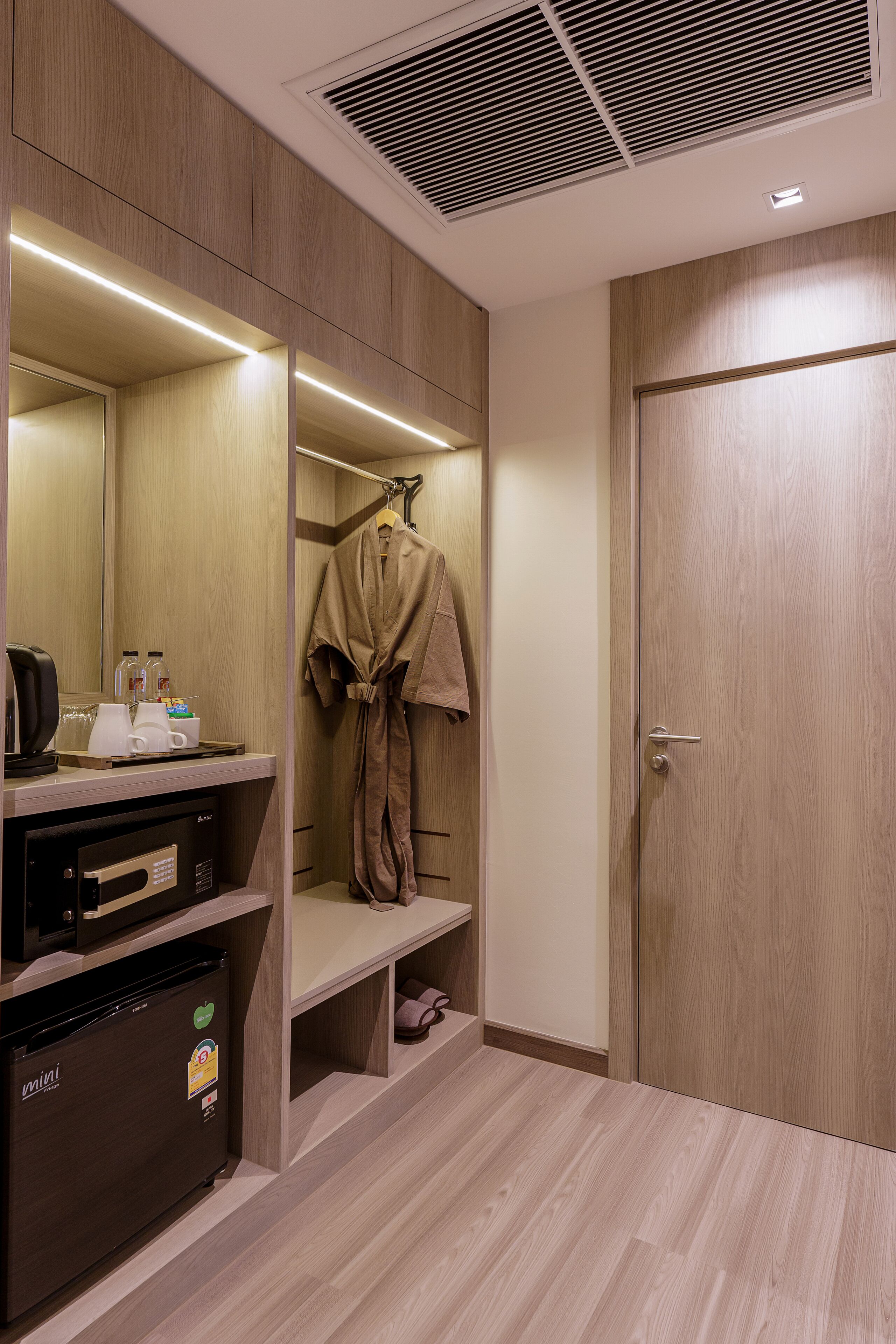 Ein modernes Badezimmer mit integriertem Minikühlschrank, einem Spiegel und einem Bademantel, der auf einem Haken hängt.