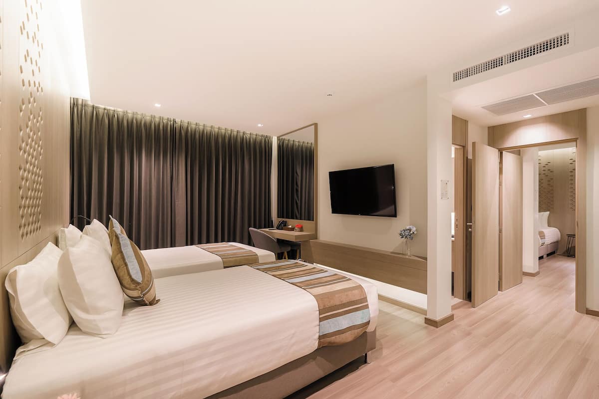 A hotel room with two beds, a desk, a TV, and a bathroom visible through an open door.