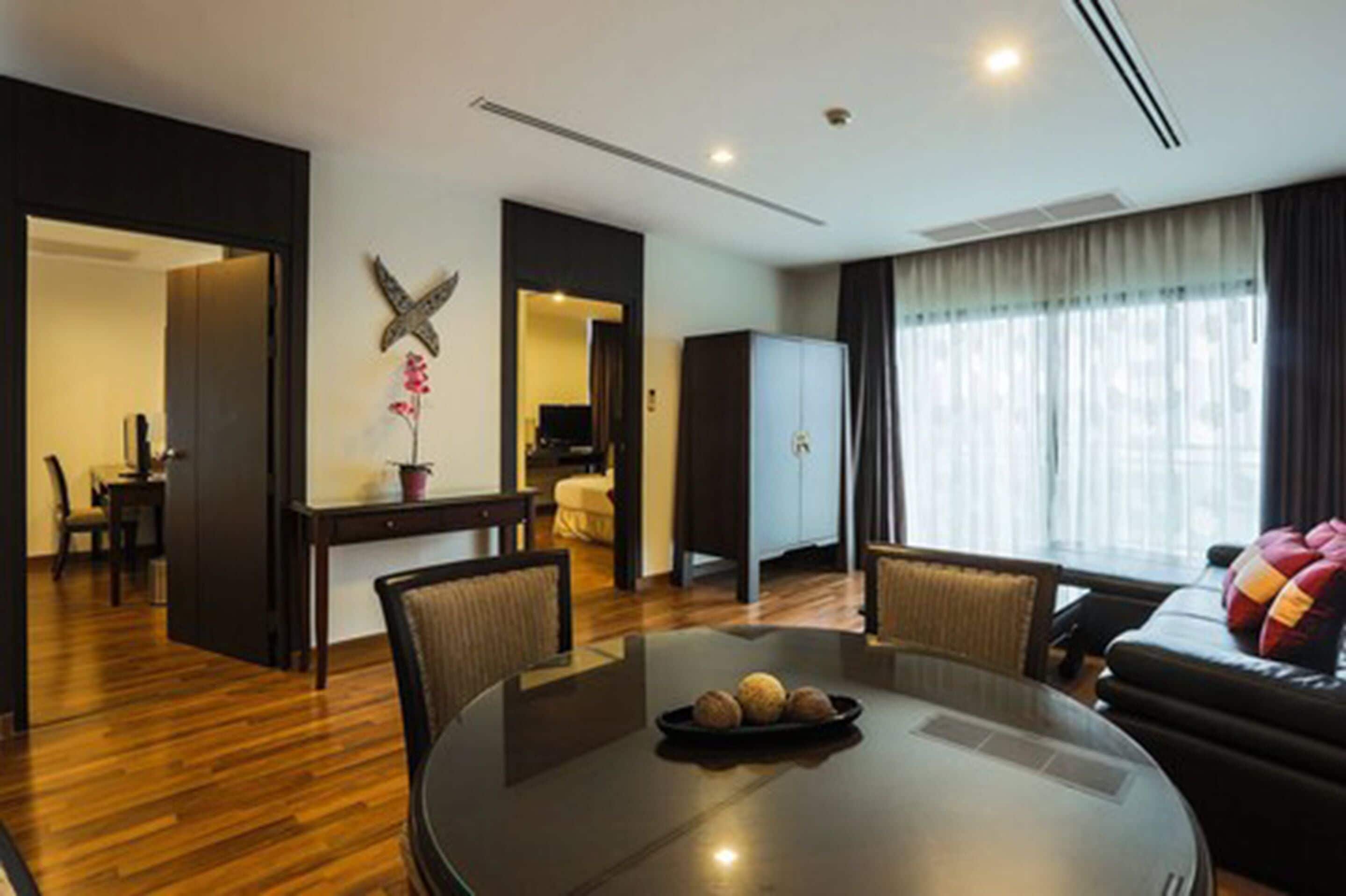 A modern hotel room with a dining area, a sofa, and a large window with curtains.