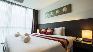 A neatly made bed with white linens and red accents, a bedside table with a lamp, and a wall-mounted artwork of three flowers.
