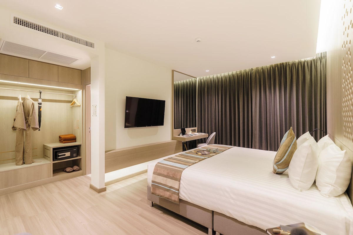 Ein modernes Hotelzimmer mit einem großen Bett, einem Flachbildfernseher, einem Schminktisch mit Spiegel und einem begehbaren Kleiderschrank.