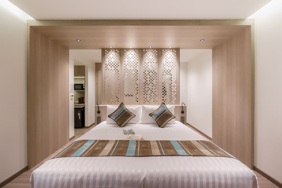A hotel room with a large bed, a wooden headboard, and a decorative screen.