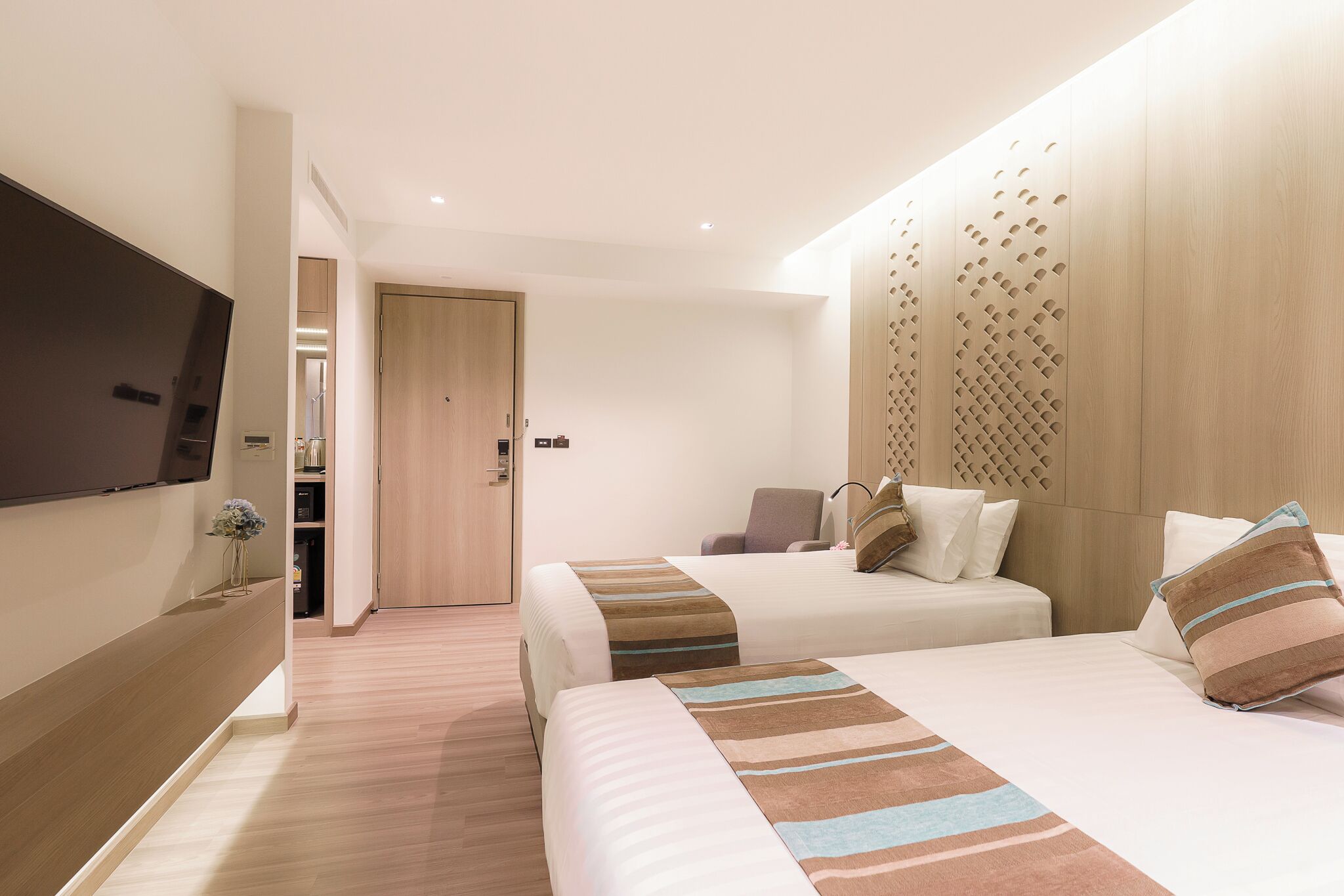 Quarto de hotel com duas camas, uma televisão, um painel de parede de madeira e uma porta que dá para um banheiro.