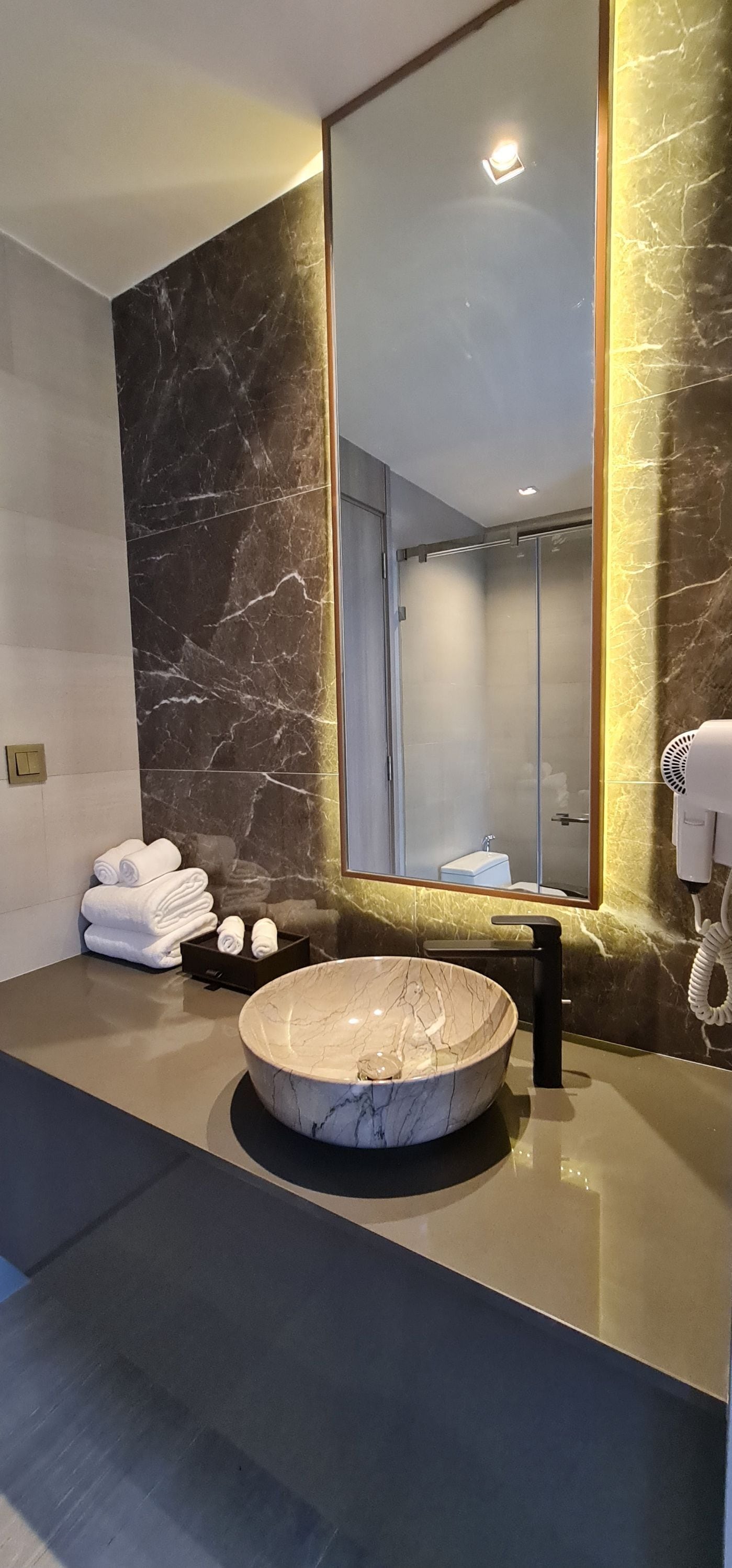 A modern bathroom with a large mirror, marble wall, and a round sink.