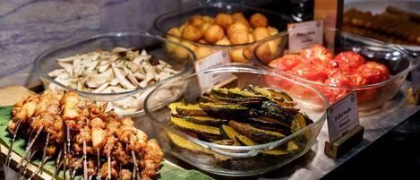A buffet with various food options including skewered meat, mushrooms, roasted potatoes, and sliced vegetables.