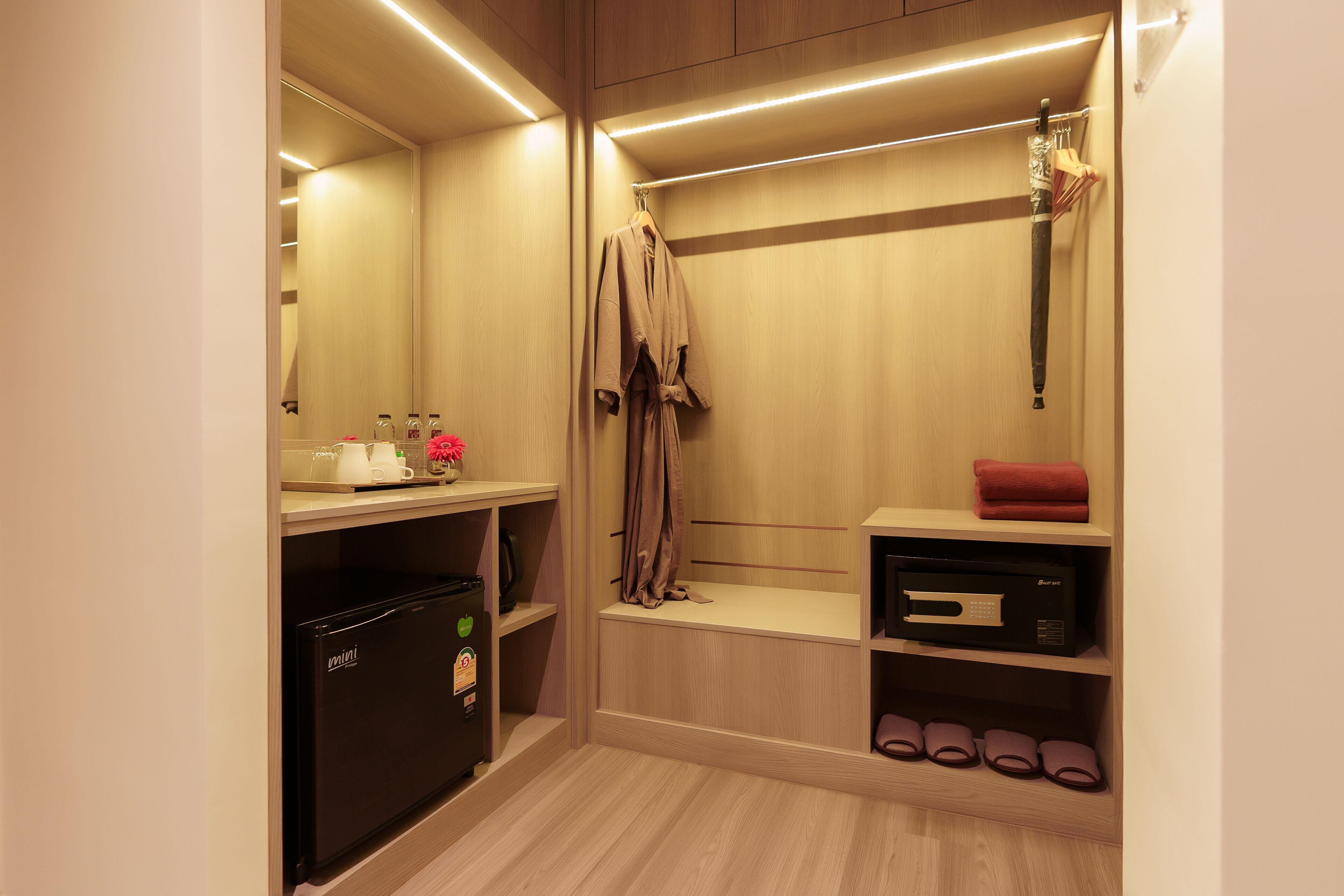 A modern bathroom with a built-in mini fridge, a vanity with a mirror, and a shower area with a towel rack.