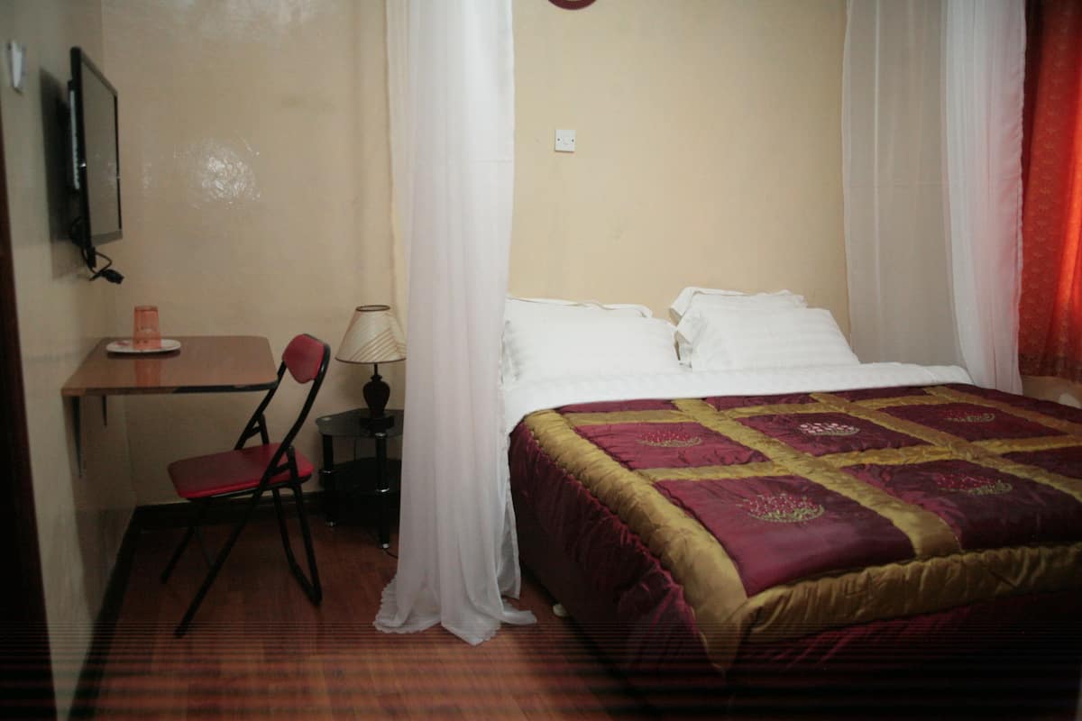 A hotel room with a bed, a desk, a chair, and a television.