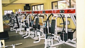 A gym with multiple exercise machines, large windows, and a yellow wall. - The Headquarters Inn (Nairobi)