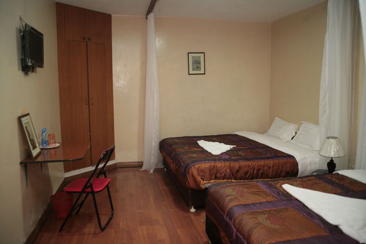 A bedroom with two beds, a wooden wardrobe, a chair, and a small table.
