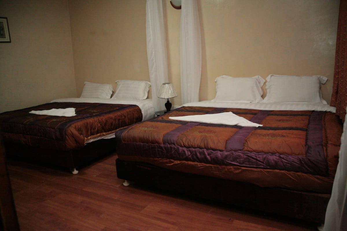 Two single beds with brown and purple bedding, a bedside table with a lamp, and a wooden floor.