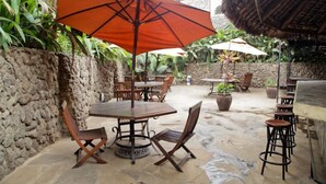 An outdoor patio area with stone walls, wooden tables, and chairs. - The Headquarters Inn (Nairobi)