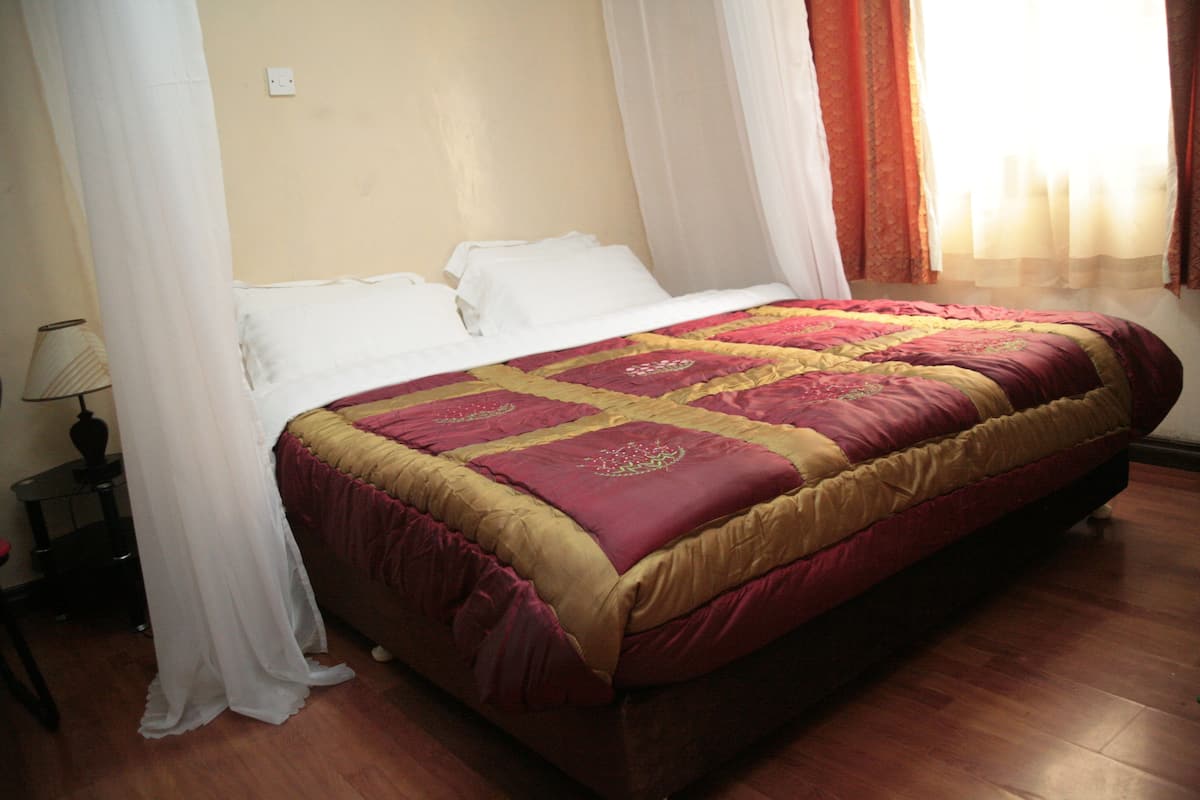 A neatly made bed with a red and gold bedspread, white pillows, and a white canopy.