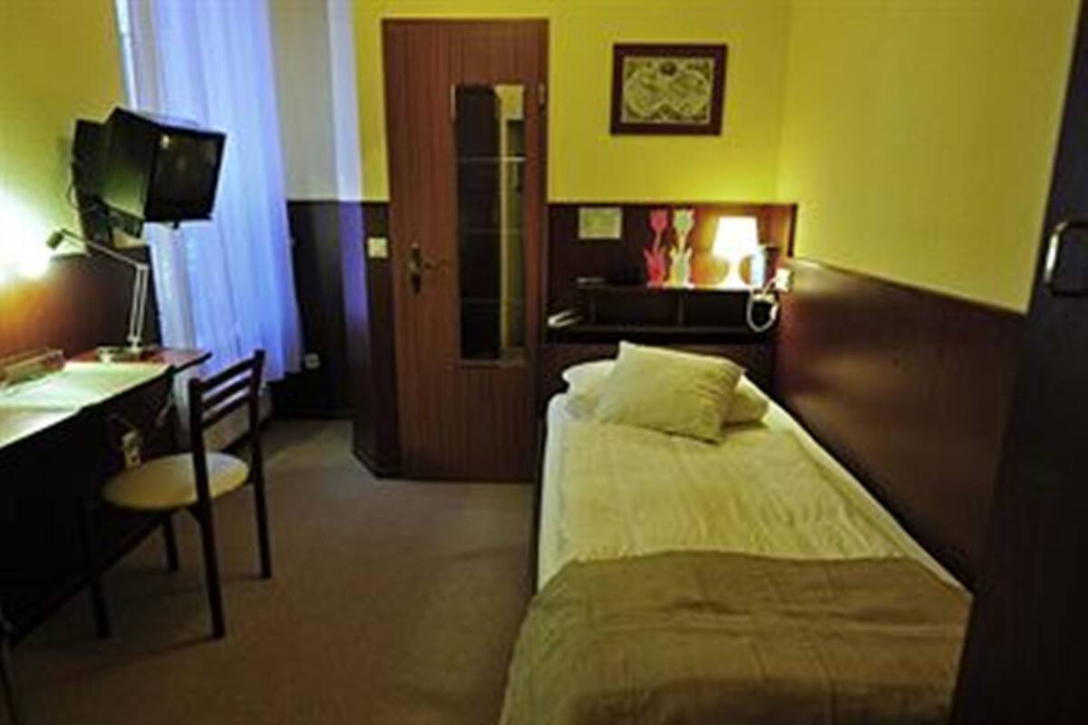 A hotel room with a bed, a desk with a chair, a television, and a nightstand with a lamp.