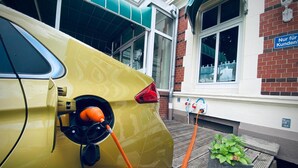 Une voiture jaune est branchée à une borne de recharge électrique devant un bâtiment sur lequel on peut lire : « Réservé aux clients ! »