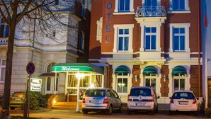 Un hôtel à la façade traditionnelle, avec une entrée accueillante et des voitures garées devant.