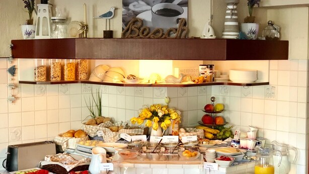 Un buffet proposant une variété de plats et de boissons, notamment des fruits, de la viande et des produits laitiers, présentés sur un comptoir dont le mur arrière est recouvert de carreaux.