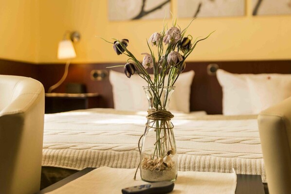Una habitación de hotel con una cama, un florero con flores y un control remoto sobre la mesita de noche.