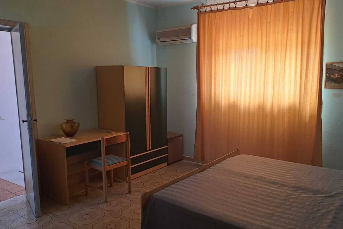 A room with a bed, a desk with a chair, a wardrobe, and a curtain.