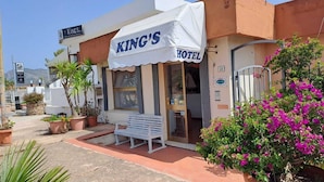 A building with a sign reading "KING'S HOTEL" and a white awning. There is a bench outside and potted plants around. - King's Hotel (Golfo Aranci)