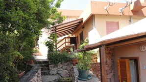 A narrow alley with stone walls, potted plants, and a small water feature. - King's Hotel (Golfo Aranci)