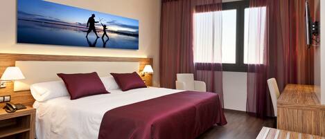 A hotel room with a large bed, two bedside tables, a desk, and a chair. There is a painting on the wall above the bed.