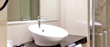 A modern bathroom with a white sink, a large mirror, a glass shower enclosure, and a black countertop.