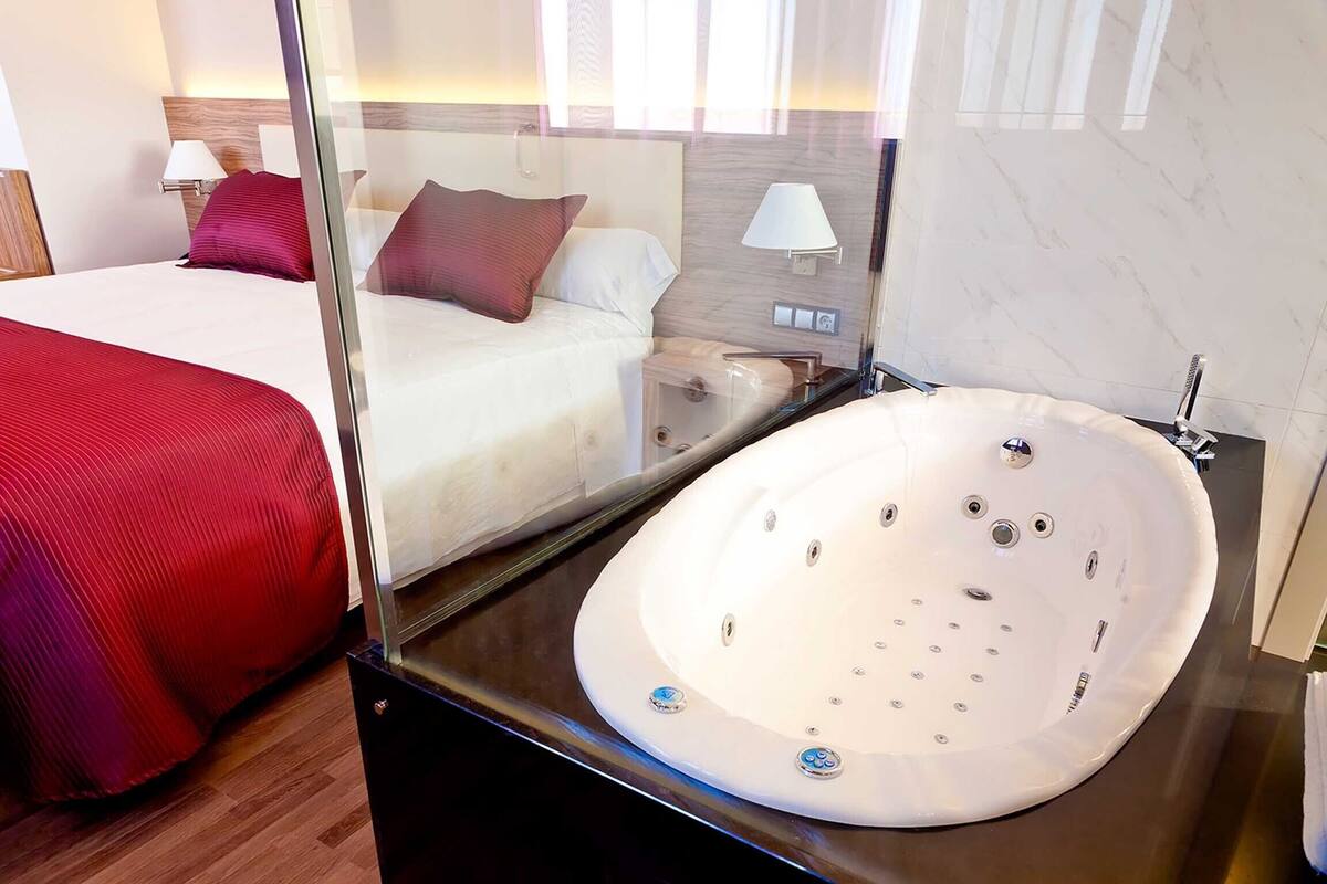 A hotel room with a large bed, a glass-enclosed jacuzzi, and a wooden headboard.