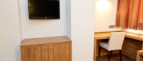 Habitación de hotel con escritorio de madera, una silla, televisor de pantalla plana montado en la pared y una mesita de noche.