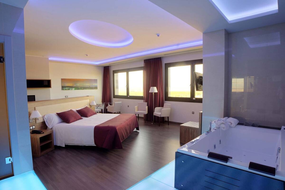 Ein modernes Hotelzimmer mit einem großen Bett, einer separaten Sitzecke, einer Whirlwanne und großen Fenstern.