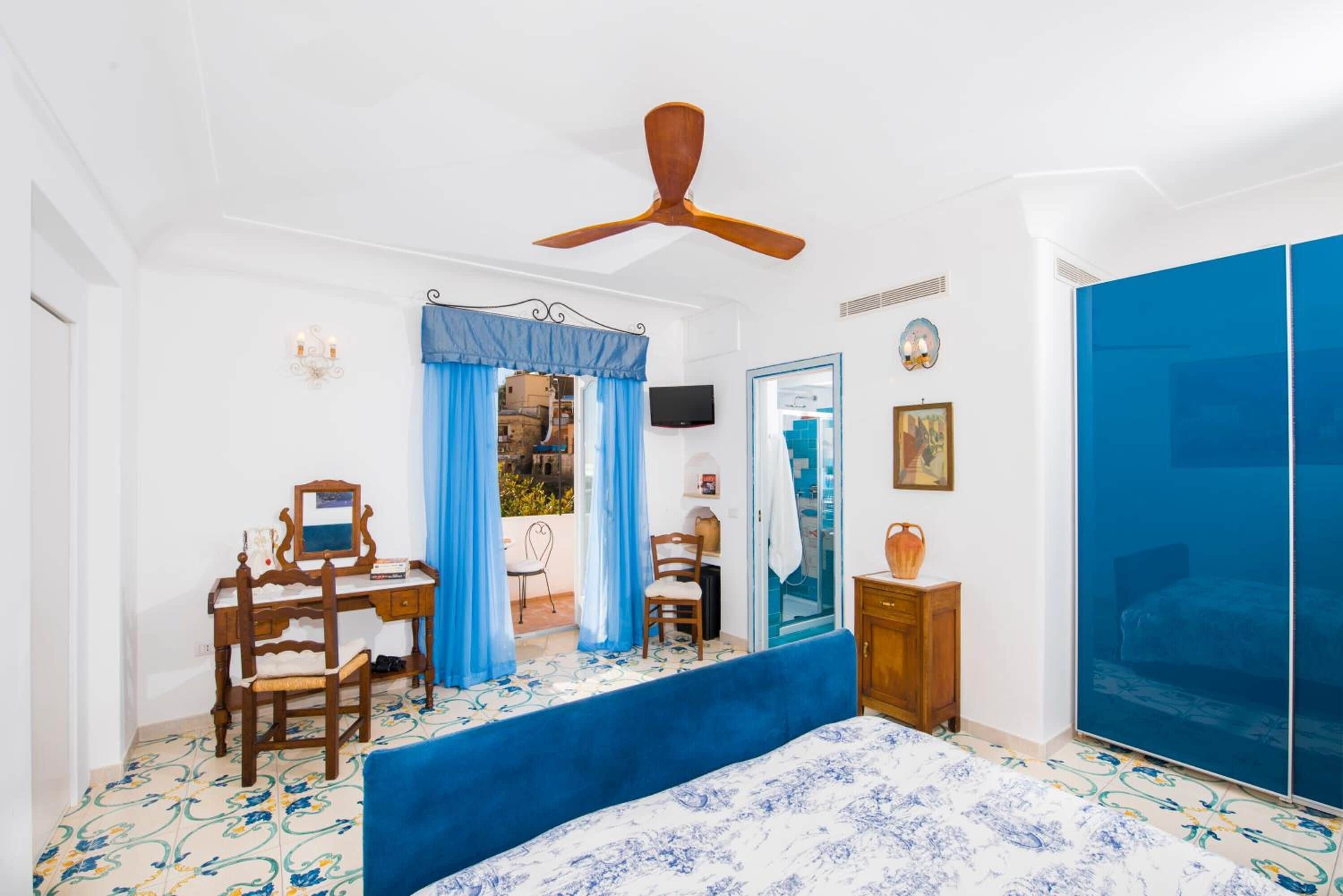 A bedroom with a bed, a desk, a chair, a ceiling fan, a TV, and a wardrobe.