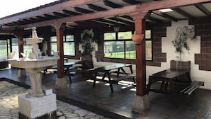An outdoor patio with stone flooring, wooden tables and benches, a decorative fountain, and potted plants. - Hotel Costa San Juan De La Canal (Santa Cruz de Bezana)